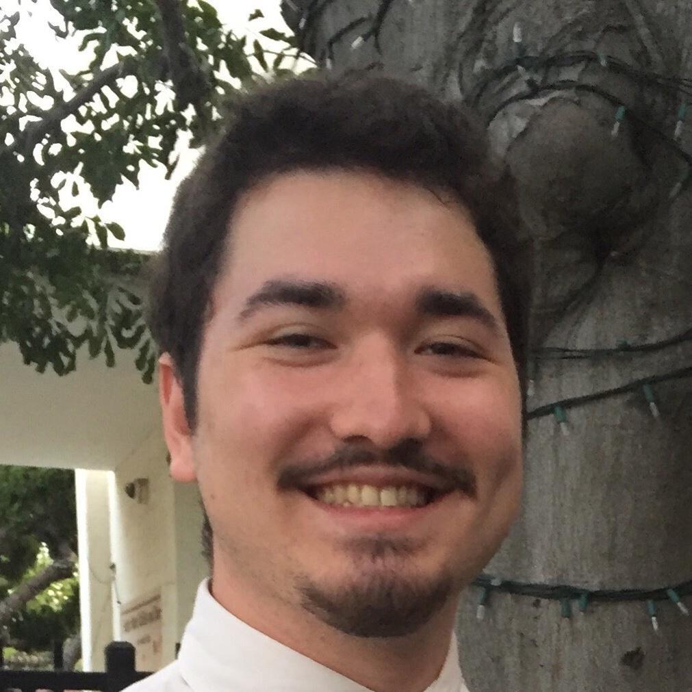 A person smiling outdoors near a tree.