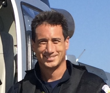 A person in a jacket smiling in front of a helicopter.