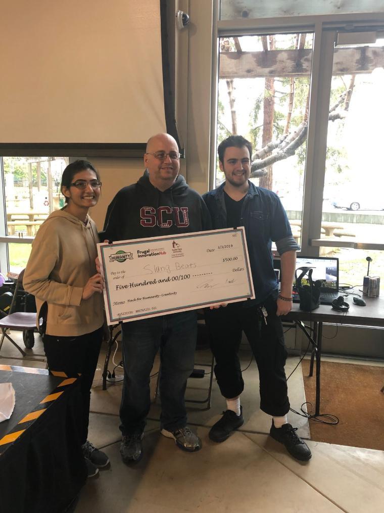 Three people holding a large check inside a room.