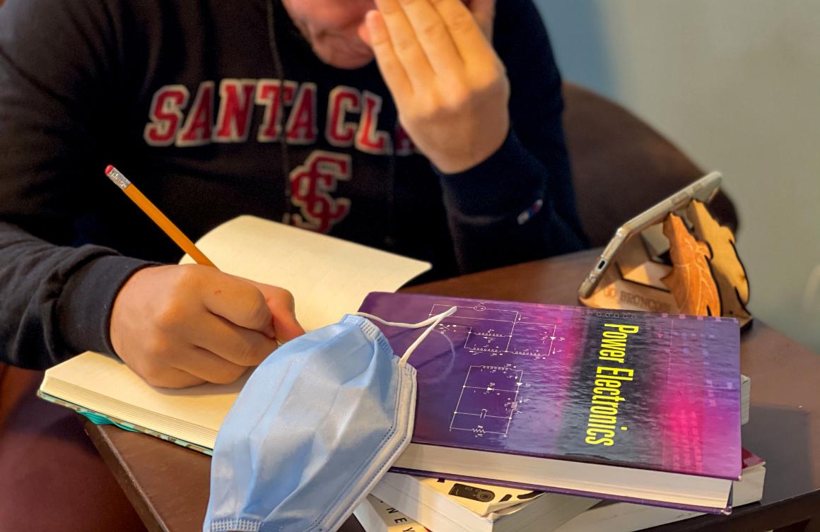 A stressed engineering student working at home with phone, mask, textbooks