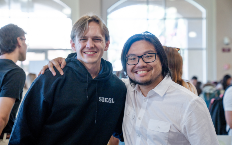 two guys standing side by side smiling at an event 