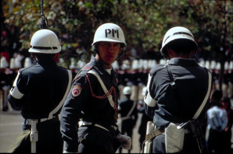 Three police officers wearing helmets in front of a crowd.