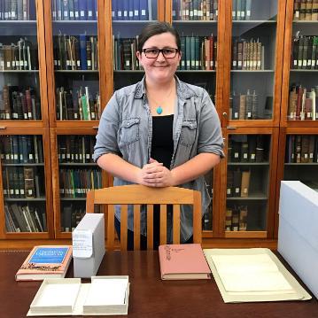 A person standing in a library with books on a table.