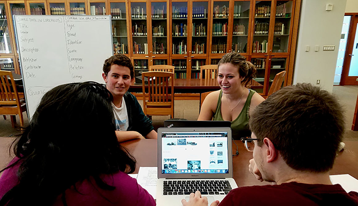 Four people having a discussion around a laptop in a library.