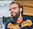 A bearded individual wearing glasses and a colorful shirt.