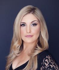 A woman with long hair, in a black outfit against a dark background.