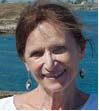 A person smiling with a background of water and rocky coast.