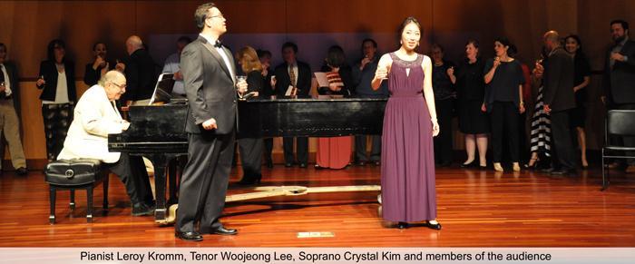 Two singers perform on stage with a pianist and an orchestra.