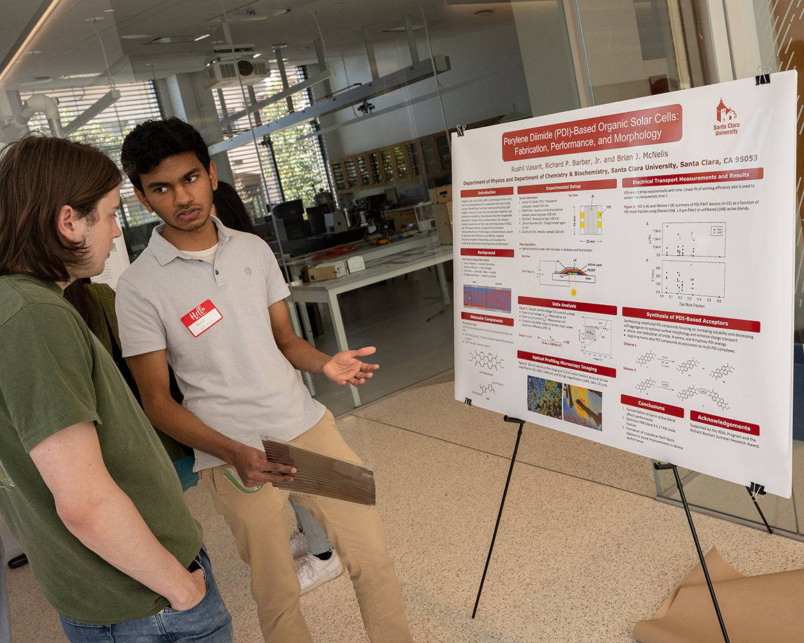 Rushil Vasant discusses his research standing next to his research poster.