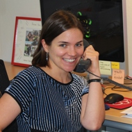 A person smiling while talking on the phone at a desk.