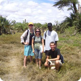 Four people standing on a path in a grassy, rural area.