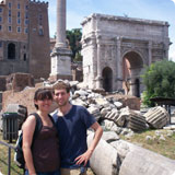 Two people standing in front of ancient Roman ruins.