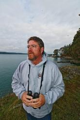 John Farnsworth standing outdoors next to a marsh holding his binoculars