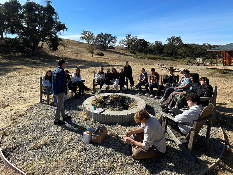 Students gathered in a semicircle outside on a sunny, blue sky day
