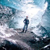 Person stands in an illuminated icy cave with blue-toned light.