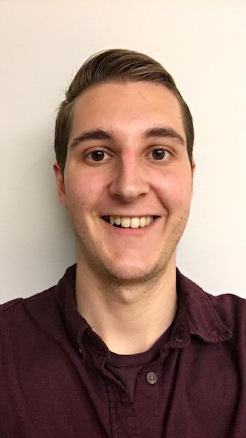 A person smiling, wearing a dark shirt against a plain background. image link to story