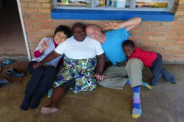 Four individuals sitting against a brick wall, smiling. image link to story