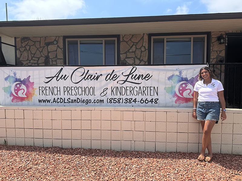 Sarah Benmalek standing next to the Au Clair de Lune banner.