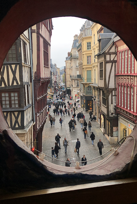 People walking in a street viewed from a round window opening.