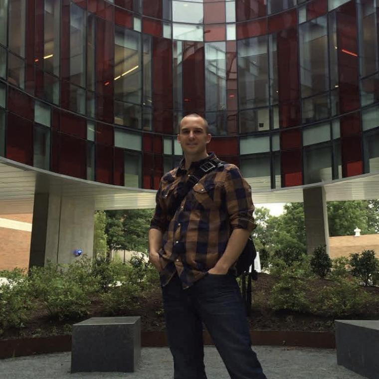 A person standing in a spacious indoor area with plants and tall windows.