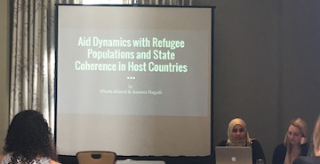 A presentation slide with text and two people seated in front.