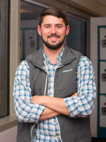 A person wearing a vest over a checked shirt smiling.