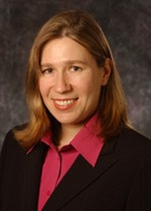 A woman in a suit with a pink shirt smiles. image link to story