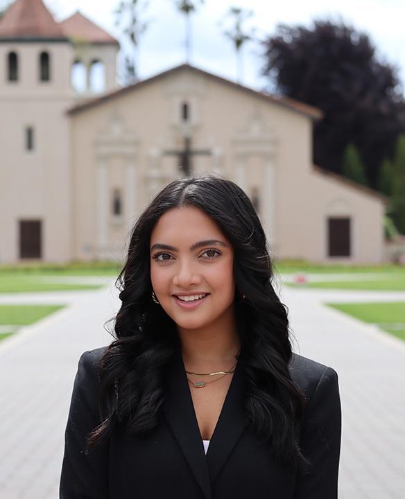 A female student wearing black standing in front of the Santa Clara Mission Church