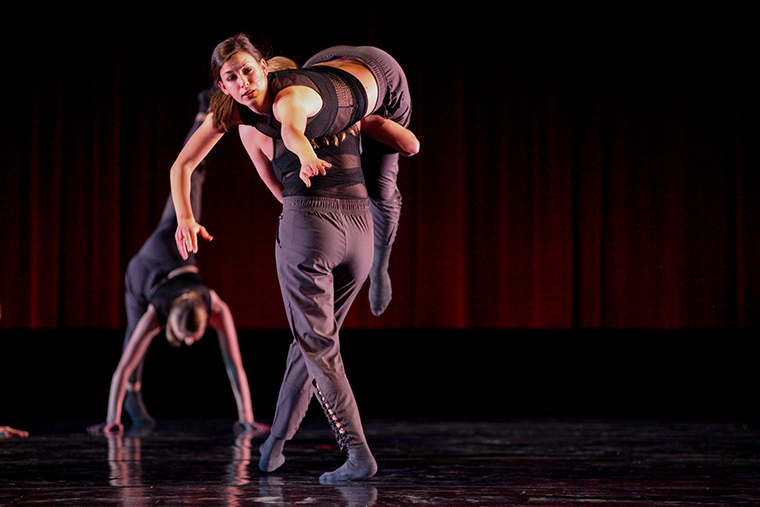 Two dancers performing an acrobatic lift on a dimly lit stage.