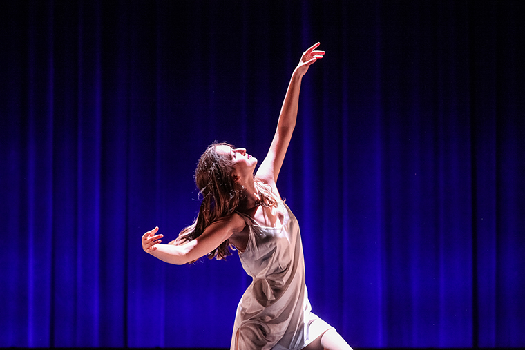 A dancer performing on stage against a blue backdrop.