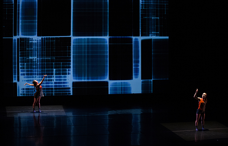 Two people performing on a dimly lit stage with blue rectangular lights.