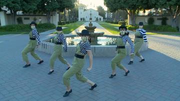 A group of dancers performs in front of a fountain in a park.