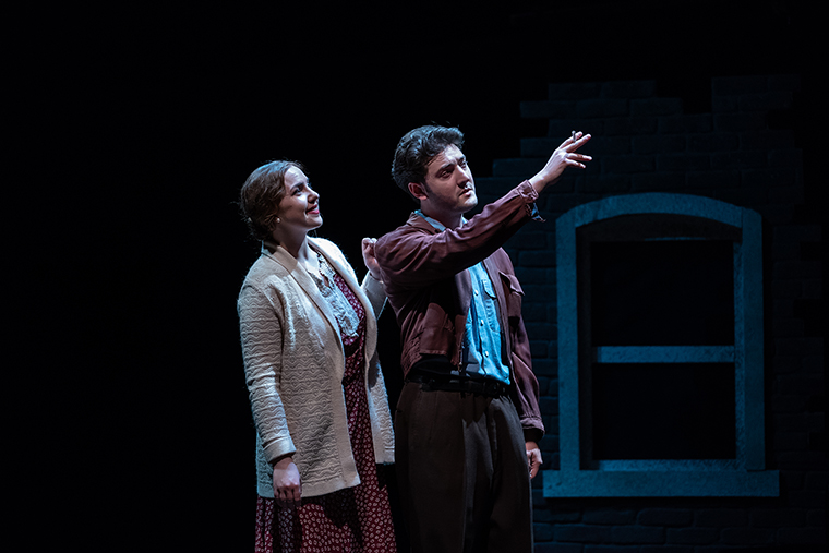 A man and woman on stage, pointing towards an object.