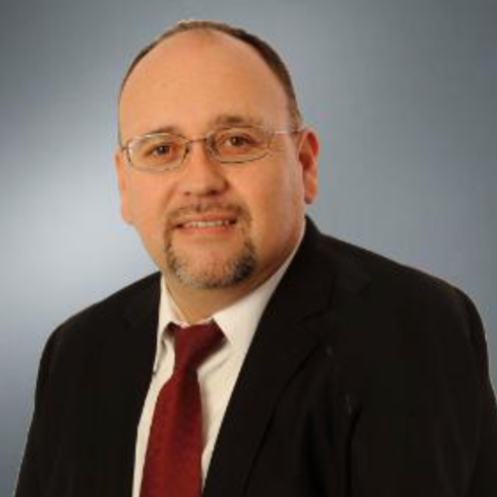 A person in a suit and tie against a gray background.