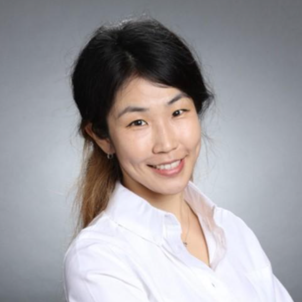 A person smiling in a white shirt against a gray background.