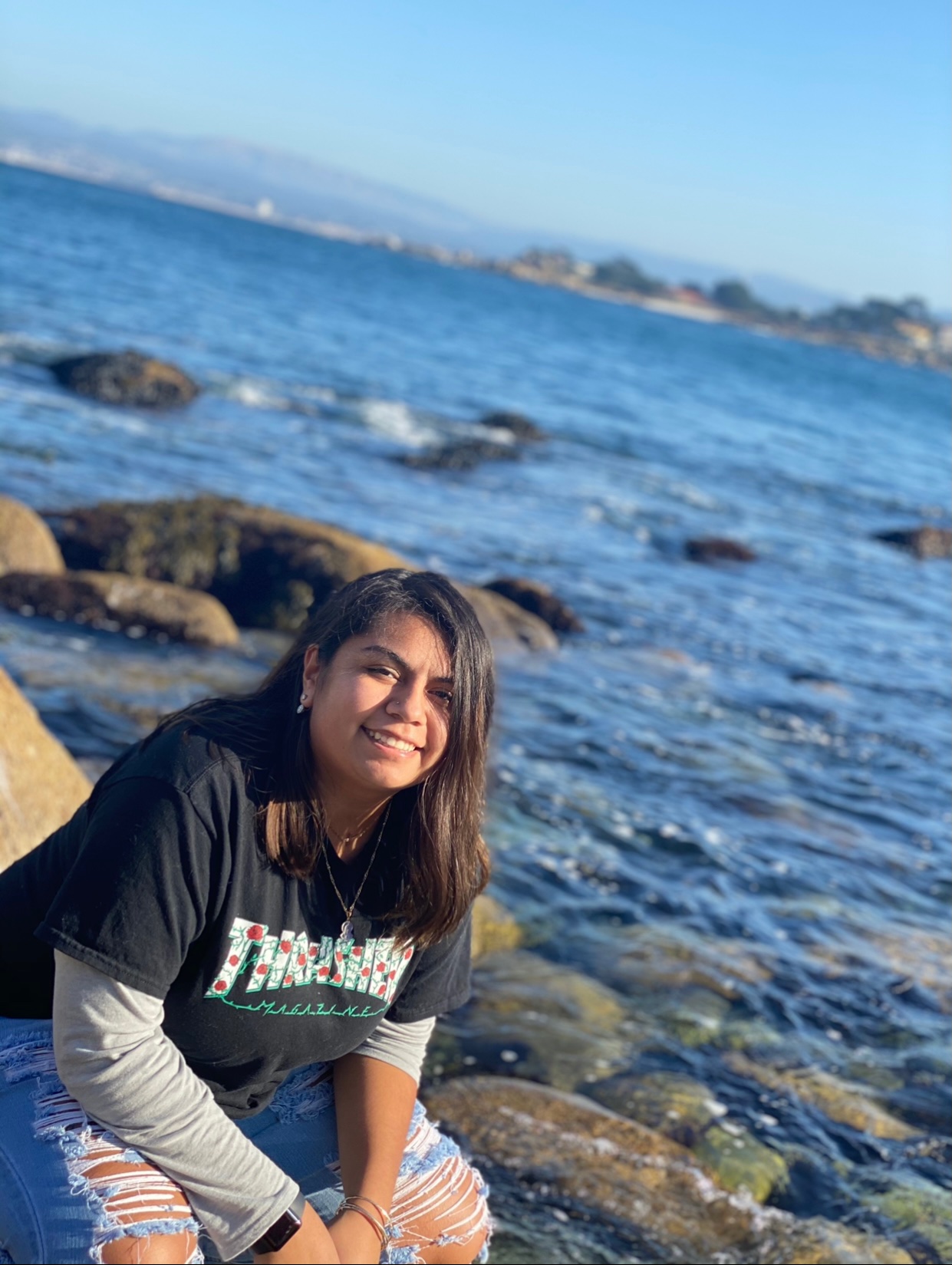 Person sitting on rocks near a coastal area with a clear blue sky.