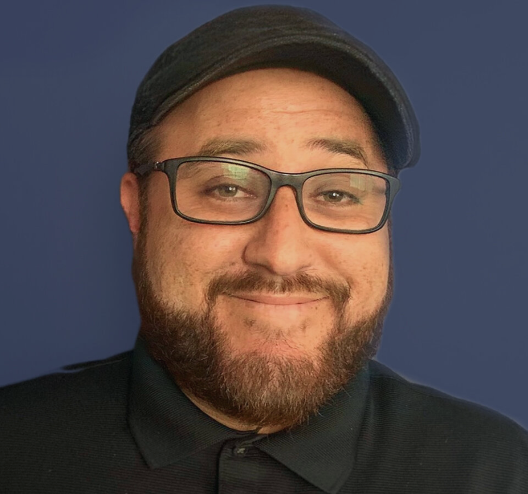 A man with glasses smiling against a blue background.