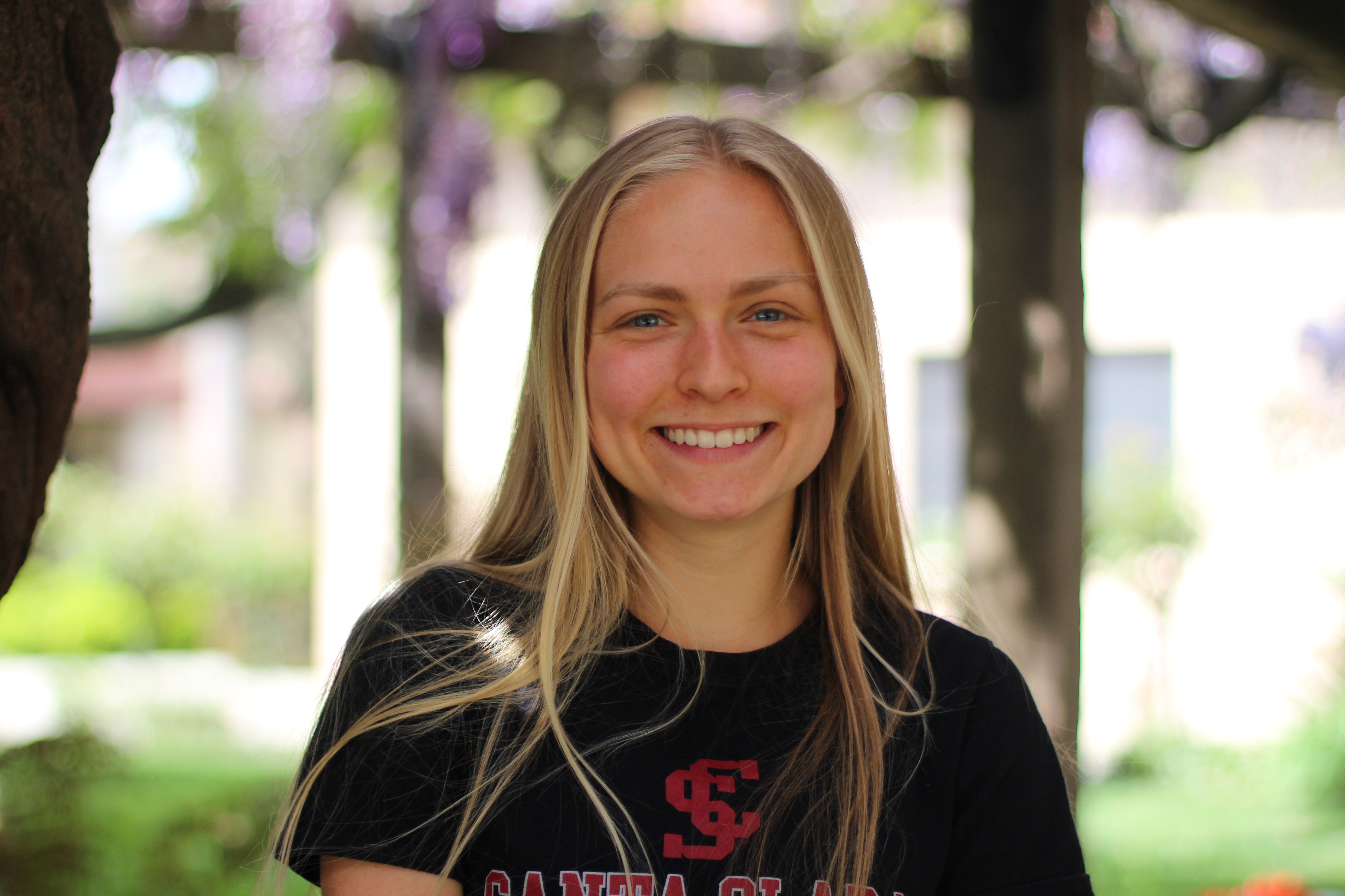 A person smiling outdoors with trees in the background.