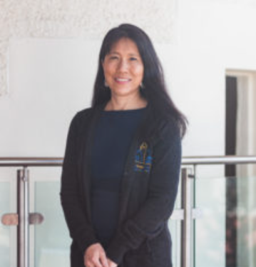 Woman standing indoors wearing a dark sweater in front of a railing.