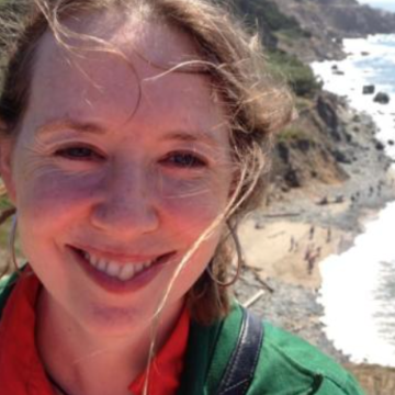 A person smiling near a rocky coastline.