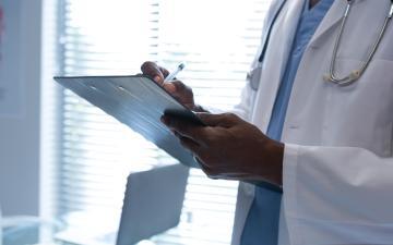 Doctor writing on a clipboard in a hospital. Image by WavebreakMediaMicro via Adobe Stock.