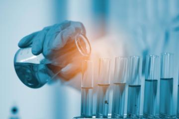 Laboratory researcher or doctor pouring solvent into a test tube.   Image by crizzystudio via Adobe Stock.