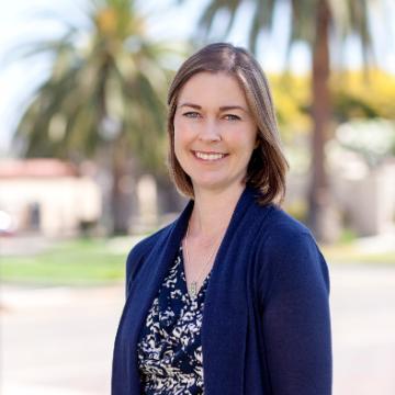 A person smiling outdoors with palm trees in the background.