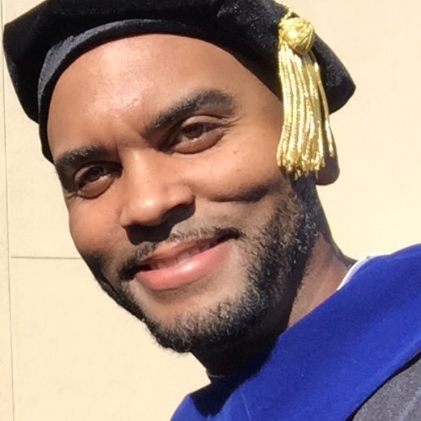 A person smiling, wearing academic regalia with a blue hood and a tassel.