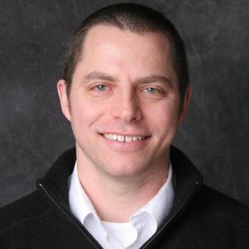 A man in a black sweater against a dark background.