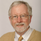 A man with glasses and a beard, wearing a beige jacket.