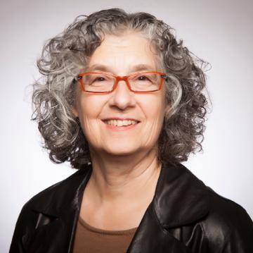 A person with glasses and curly hair smiles against a plain background.