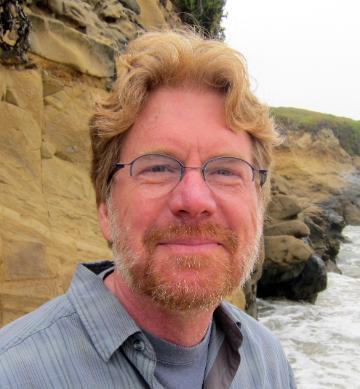 A person is smiling near a rocky shoreline.