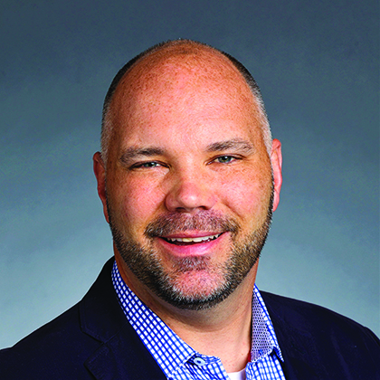 A person in a suit smiling against a gray background.