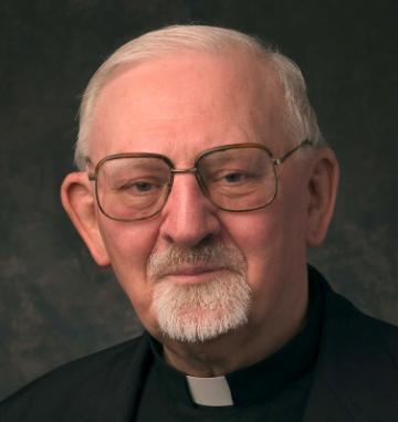 A man smiling, dressed in clerical attire with glasses.